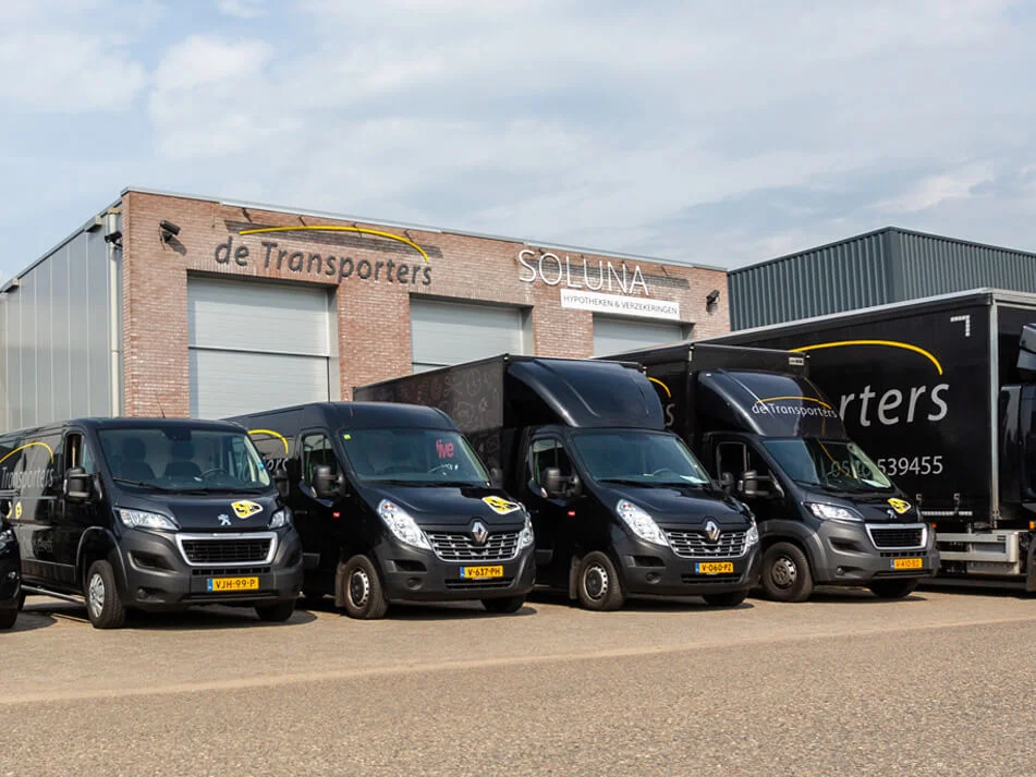 Vloot van bedrijfswagens van De Transporters, bestaande uit bestelwagens en vrachtwagens, geparkeerd voor het bedrijfspand in Almelo.