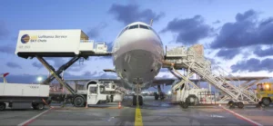 Vrachtvliegtuig op het platform van een luchthaven tijdens belading, met catering- en laadvoertuigen van Lufthansa Service Sky Chefs aan weerszijden van het toestel.